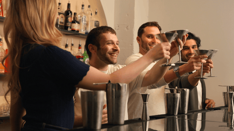 Group of people at a bar raising their cocktail glasses in a toast.