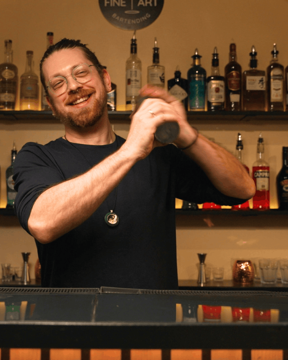 Smiling student shaking a cocktail behind the bar at Fine Art Bartending School