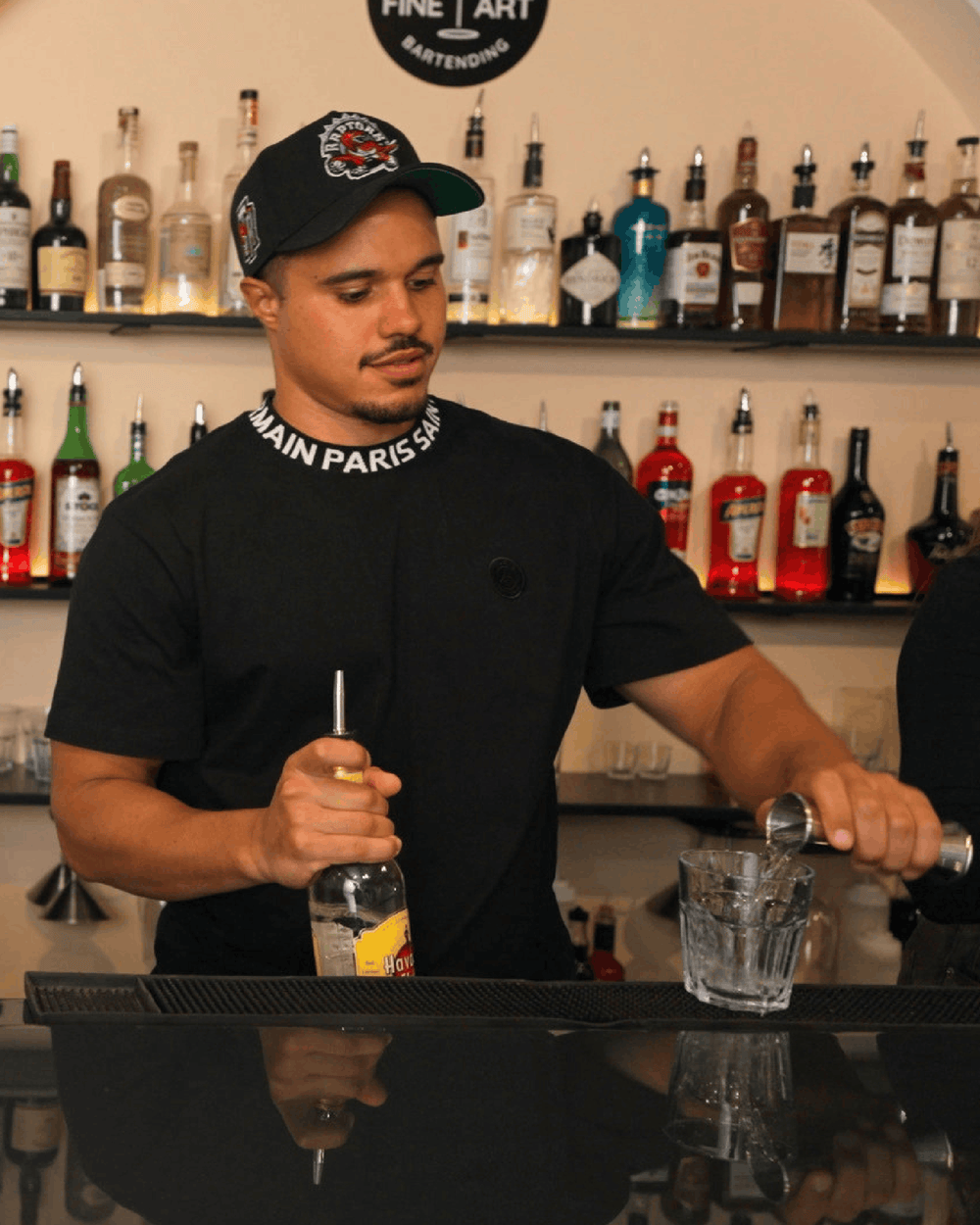 Bartending student measuring a pour with a jigger behind the bar