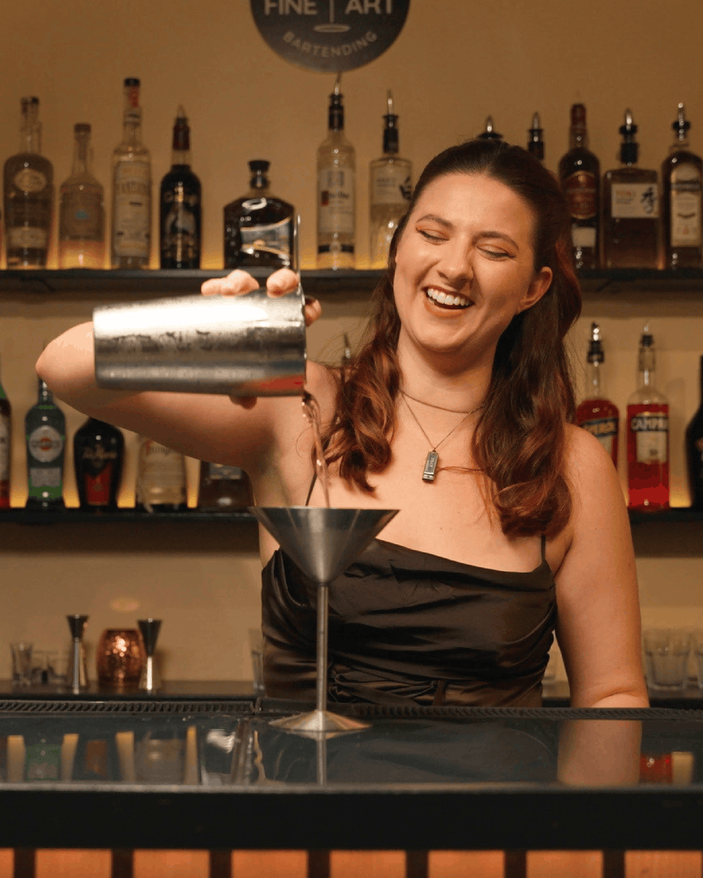 Bartender pouring a cocktail from a shaker into a martini glass at Fine Art Bartending School