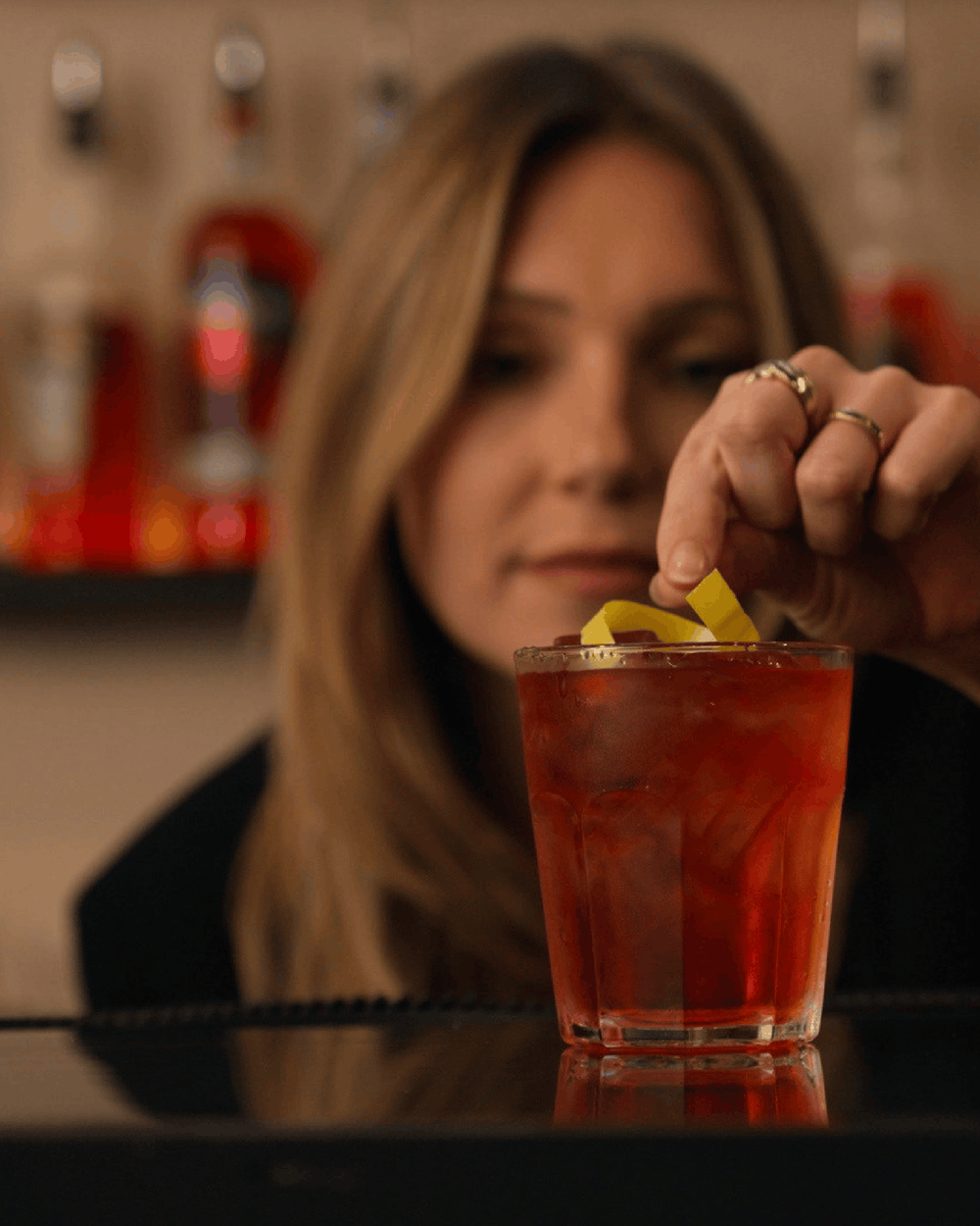 Bartender garnishing a red cocktail with an orange twist