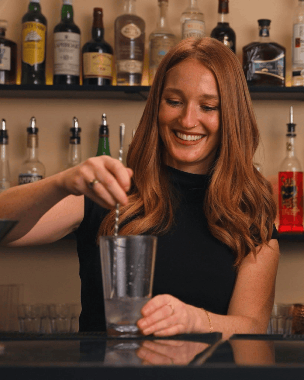 Bartending student stirring a cocktail in a mixing glass behind the bar