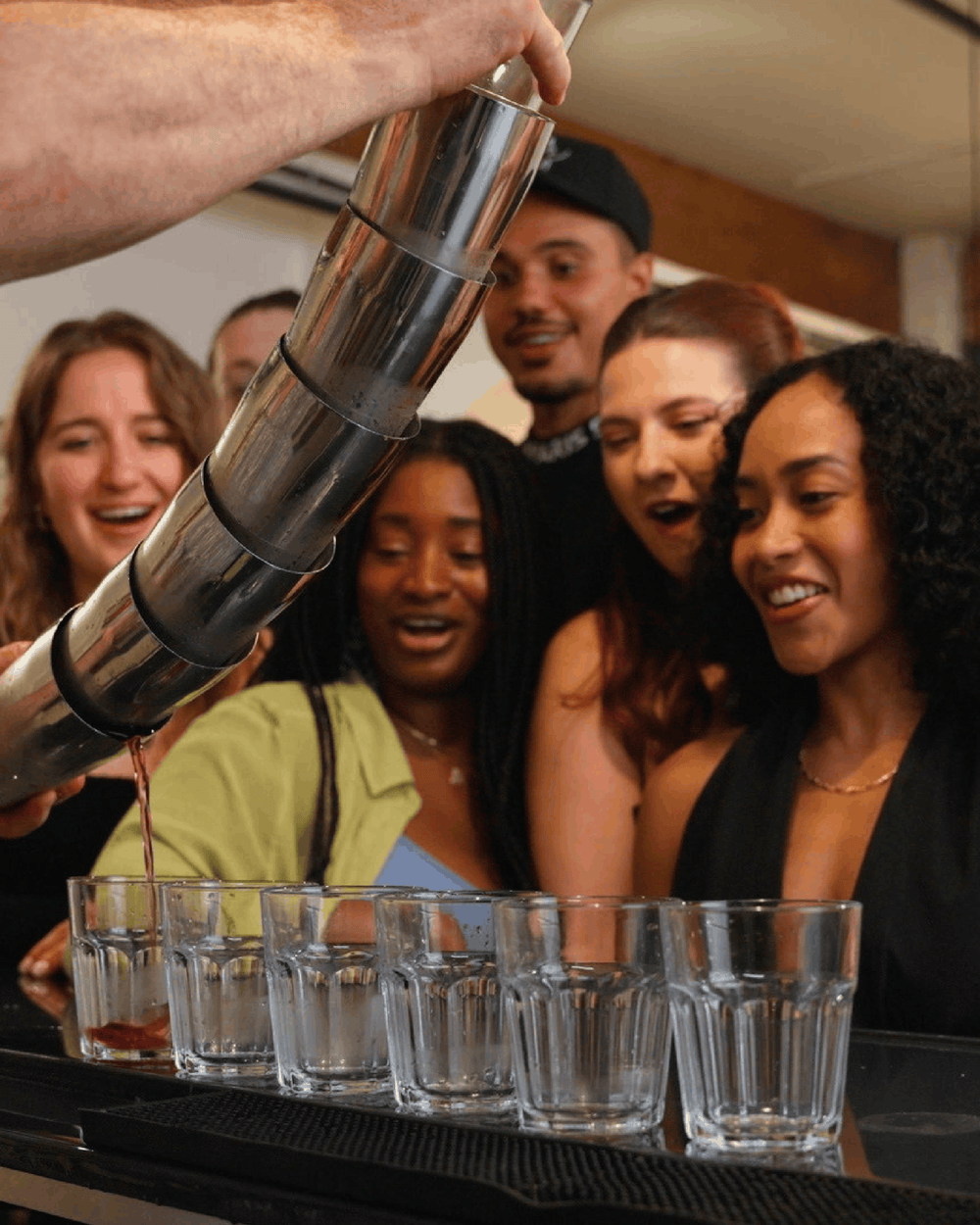 Group of smiling students watching an instructor pour a cocktail at Fine Art Bartending School
