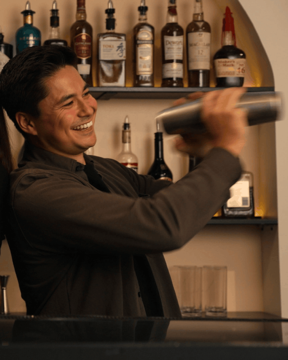 Smiling bartending student shaking a cocktail behind the bar